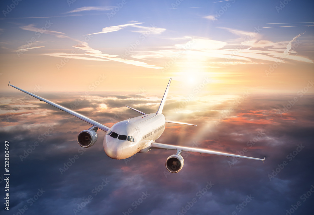 Airplane flying above clouds in dramatic sunset