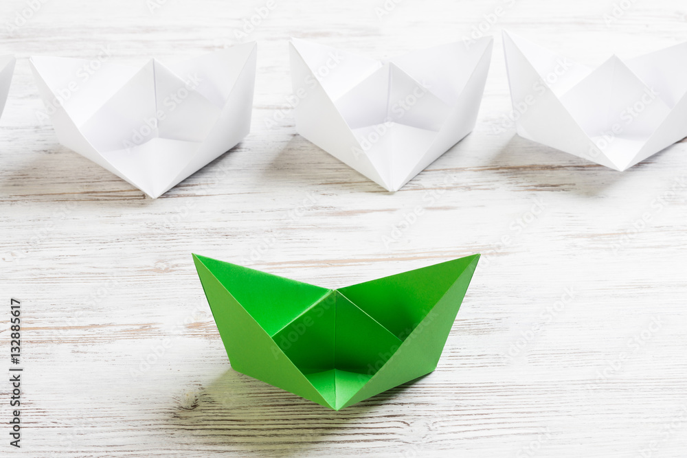 Business leadership concept with white and color paper boats on wooden table