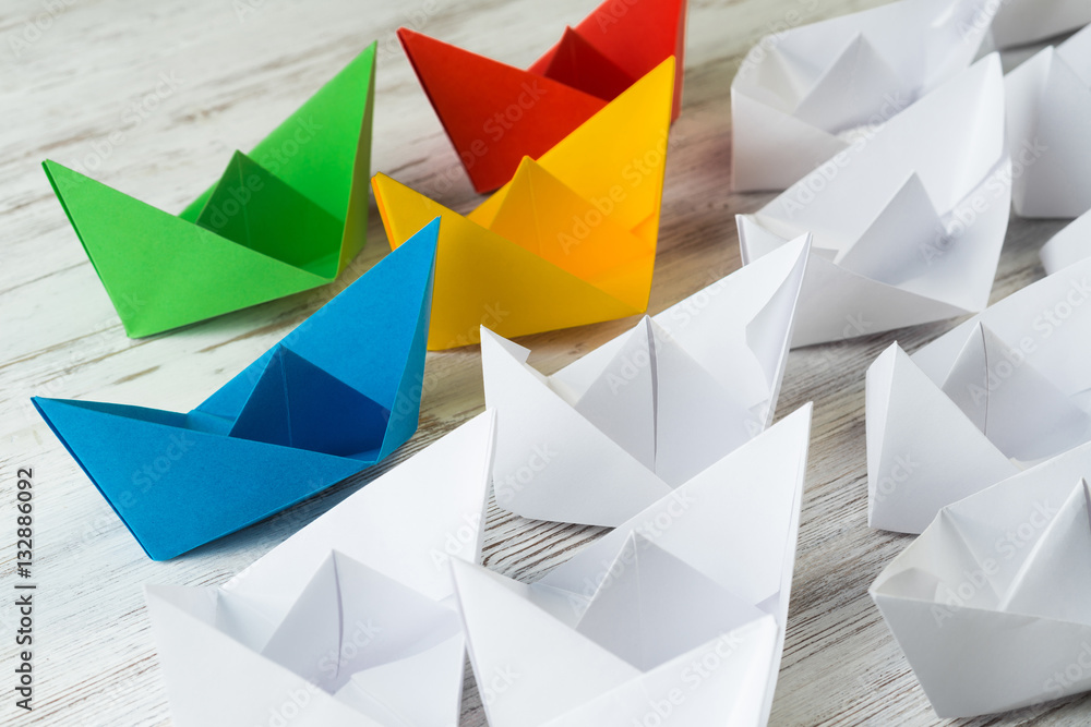 Business leadership concept with white and color paper boats on wooden table