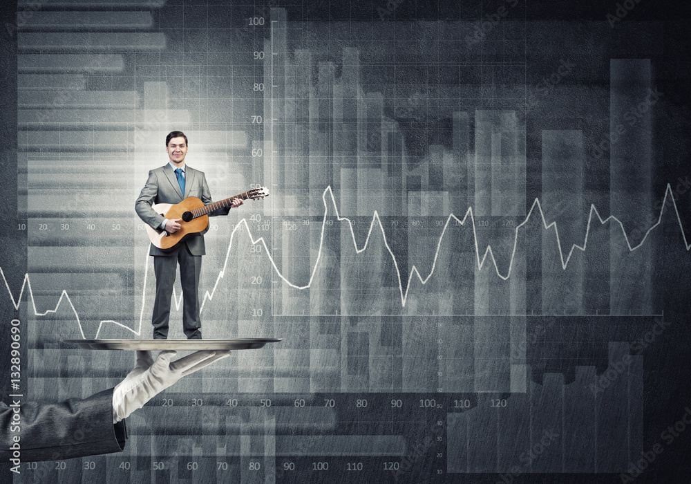 Businessman on metal tray playing acoustic guitar against concrete wall background with charts