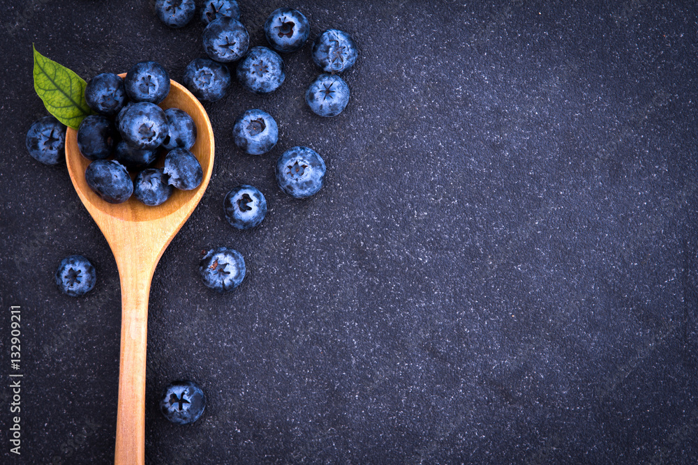  fresh picked blueberries in wooden spoon on black stone 