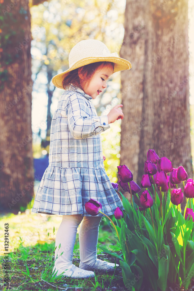 Toddler girl in a hat playing with tulips