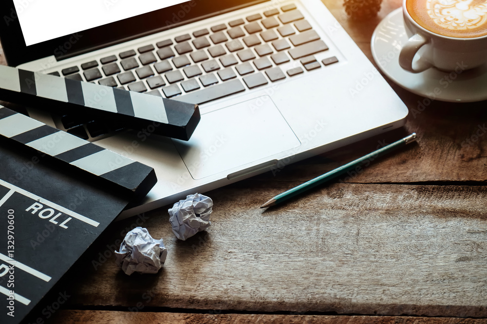 office stuff with Movie clapper laptop and coffee cup pen notepad on the wood table top view shot.
