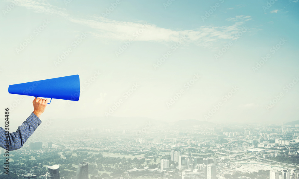 Hand of woman holding blue paper trumpet against cityscape background