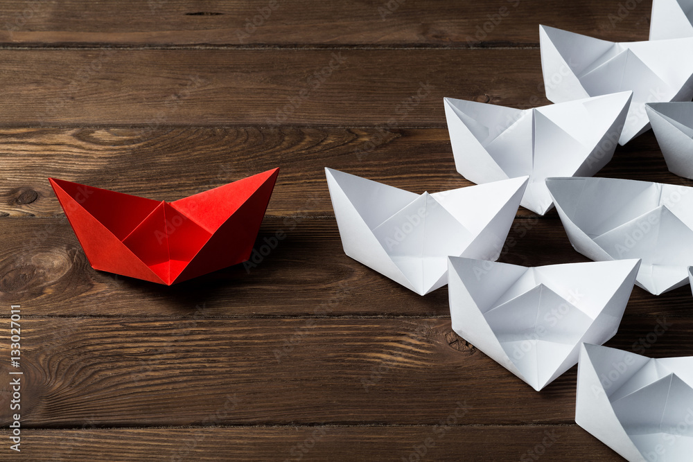 Business leadership concept with white and color paper boats on wooden table