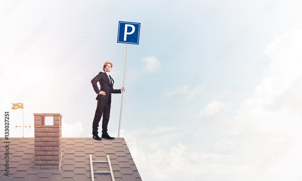 Young businessman with parking sign standing on brick roof. Mixe