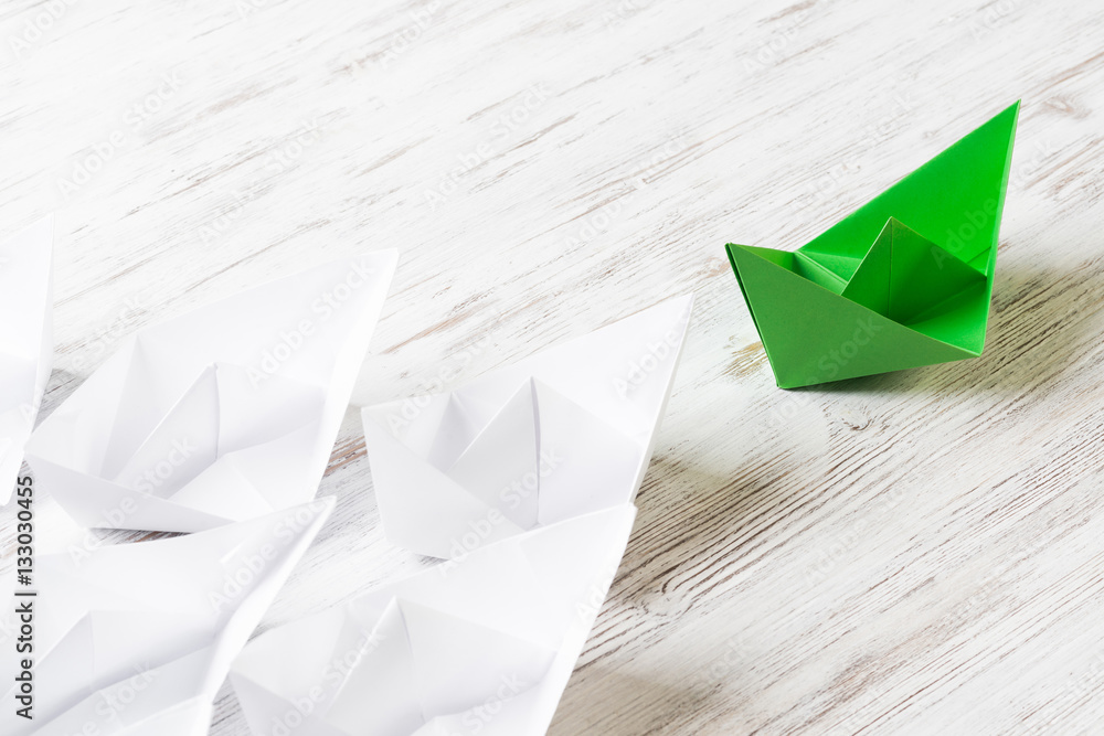 Business leadership concept with white and color paper boats on wooden table