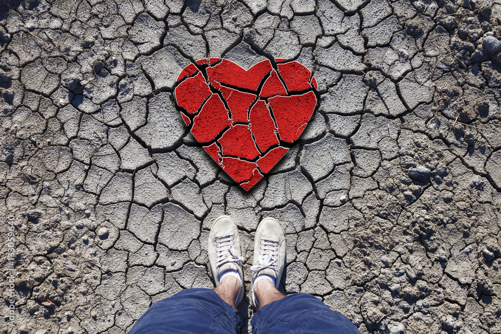 Lonely man standing on dried soil ground with illustrated cracked heart symbol. Conceptual broken lo