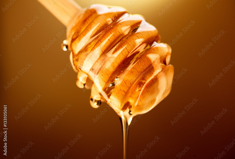 Honey dripping from honey dipper isolated on brown. Thick honey dipping from the wooden honey spoon