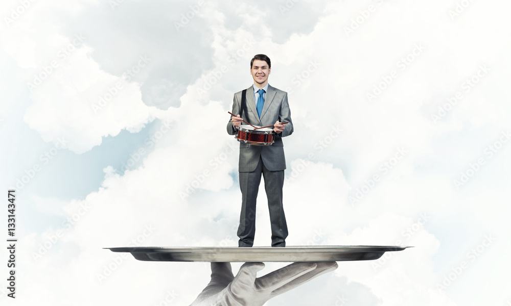 Businessman on metal tray playing drum blue sky background