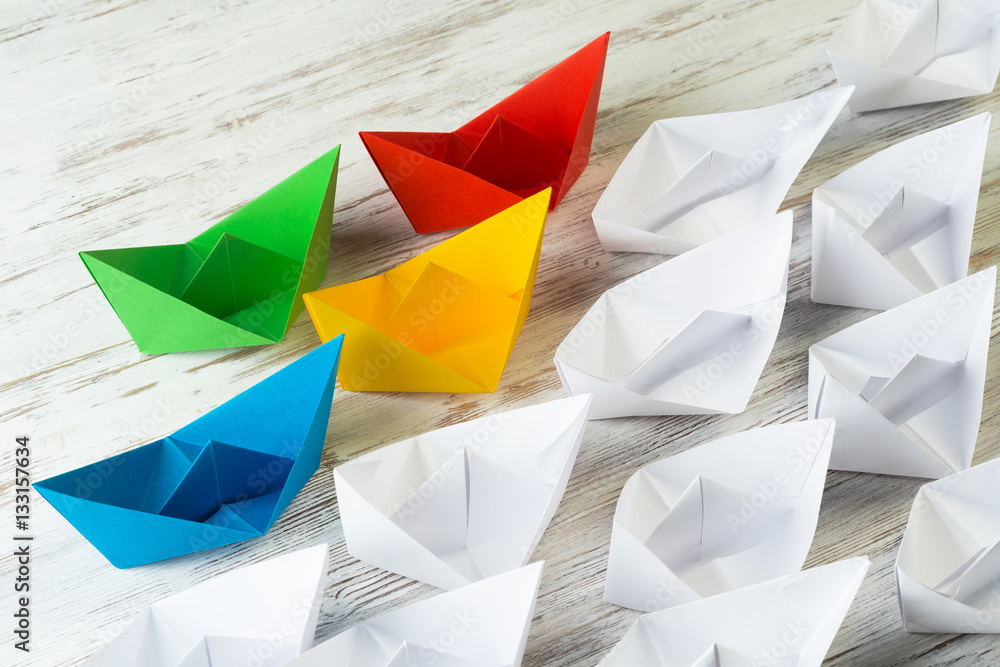 Business leadership concept with white and color paper boats on wooden table