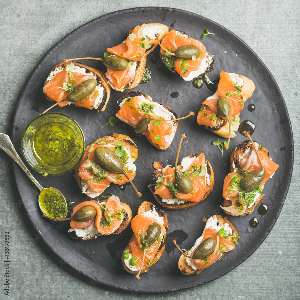 Homemade salmon crostini with cream-cheese, watercress, capers and pesto suace in round black slate 