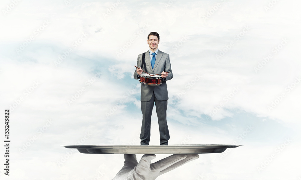 Businessman on metal tray playing drum blue sky background