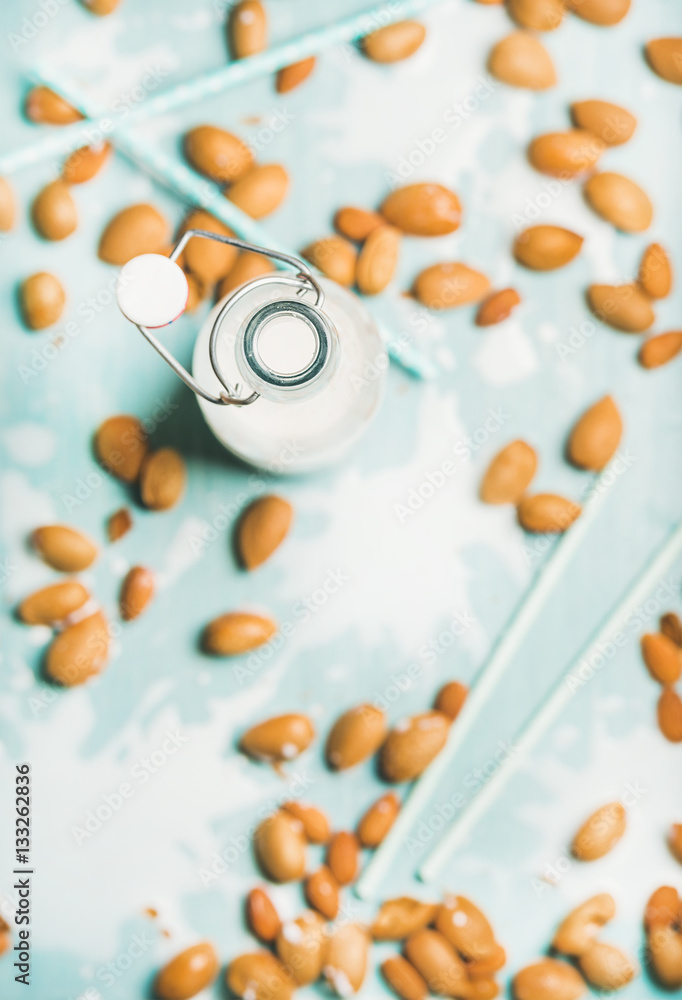 Dairy alternative milk. Almond milk in bottle and fresh nuts over blue background, top view, selecti