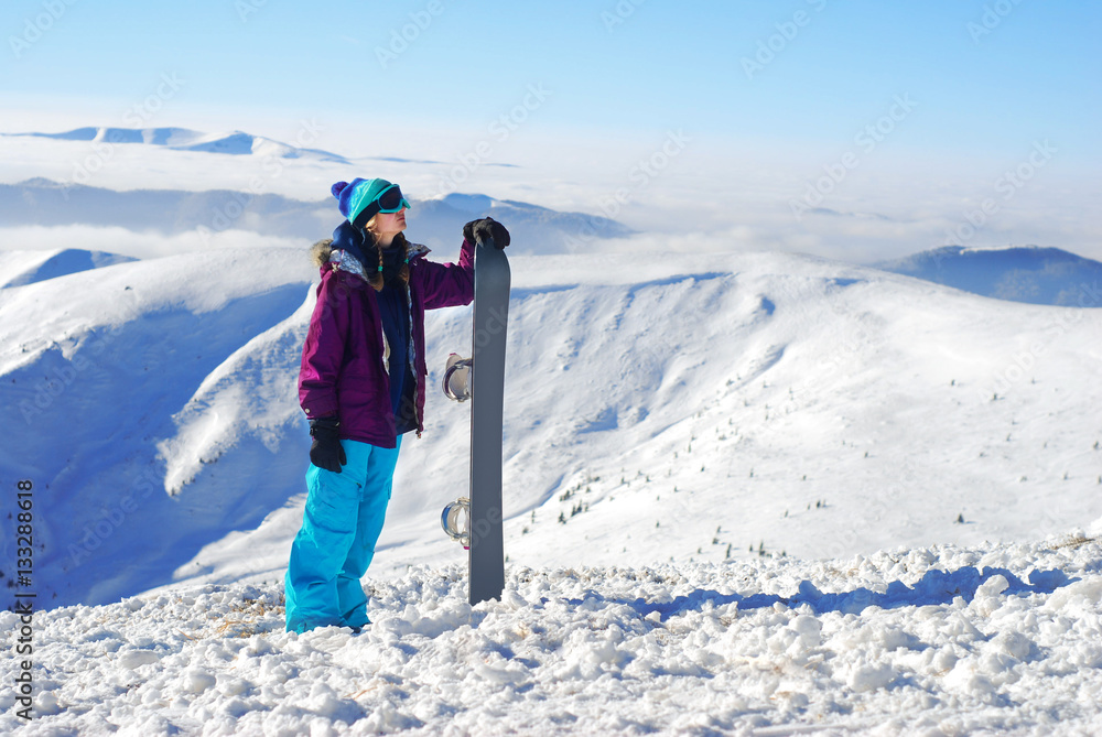 girl standing on a mountain top with snowboard in the hands