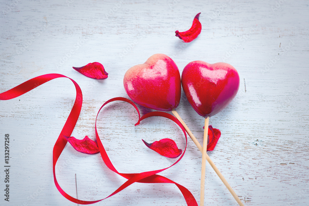 Valentines Day. Elegant red satin gift ribbon and couple of red hearts over white wooden background