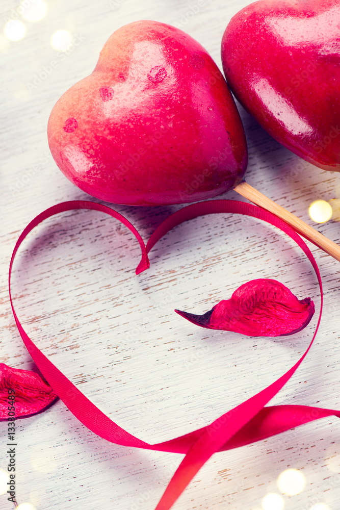 Valentines Day. Elegant red satin gift ribbon and couple of red hearts over white wooden background