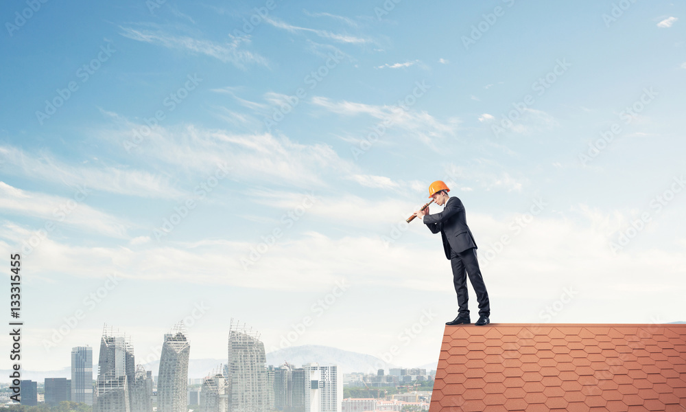 Engineer man standing on roof and looking in spyglass. Mixed med