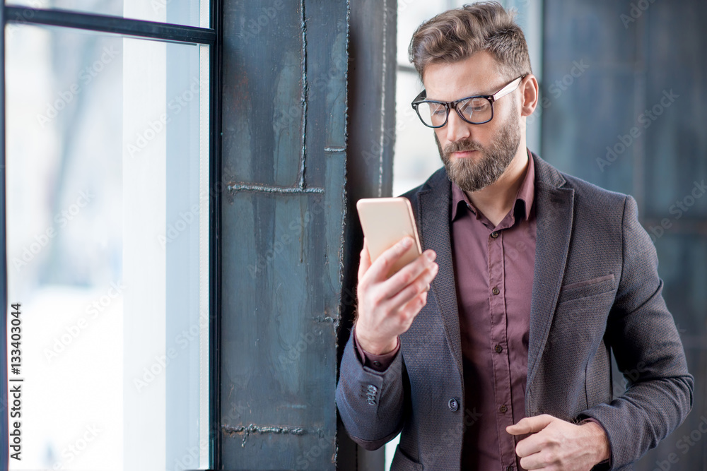 Handsome caucasian businessman dressed in the suit reading with his smart phone near the window in t