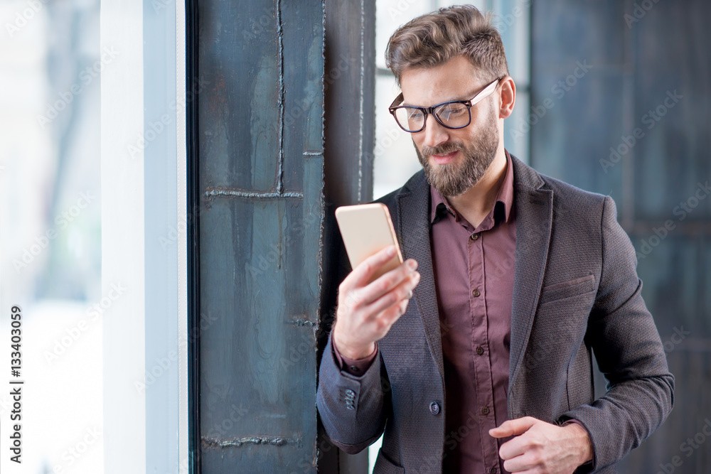 Handsome caucasian businessman dressed in the suit reading with his smart phone near the window in t