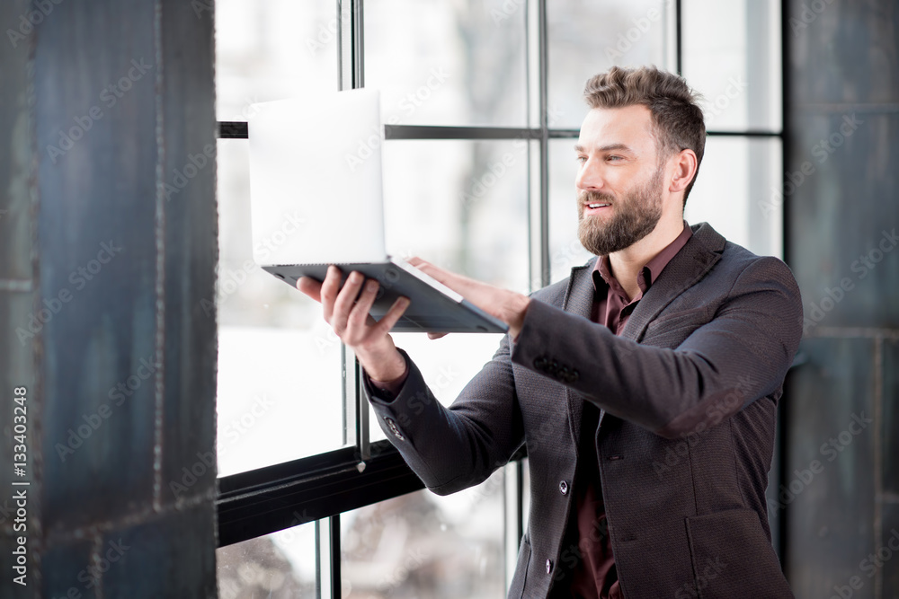 Handsome bearded businessman dressed in the suit trying to get internet connection with laptop near 