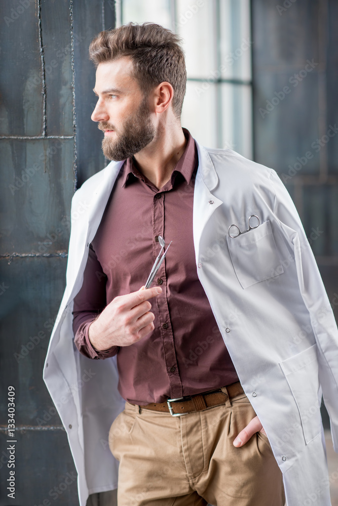 Portrait of handsome confident dentist with medical gown and dental tools standing near the window i