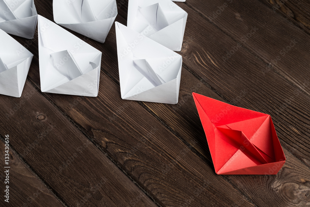 Business leadership concept with white and color paper boats on wooden table