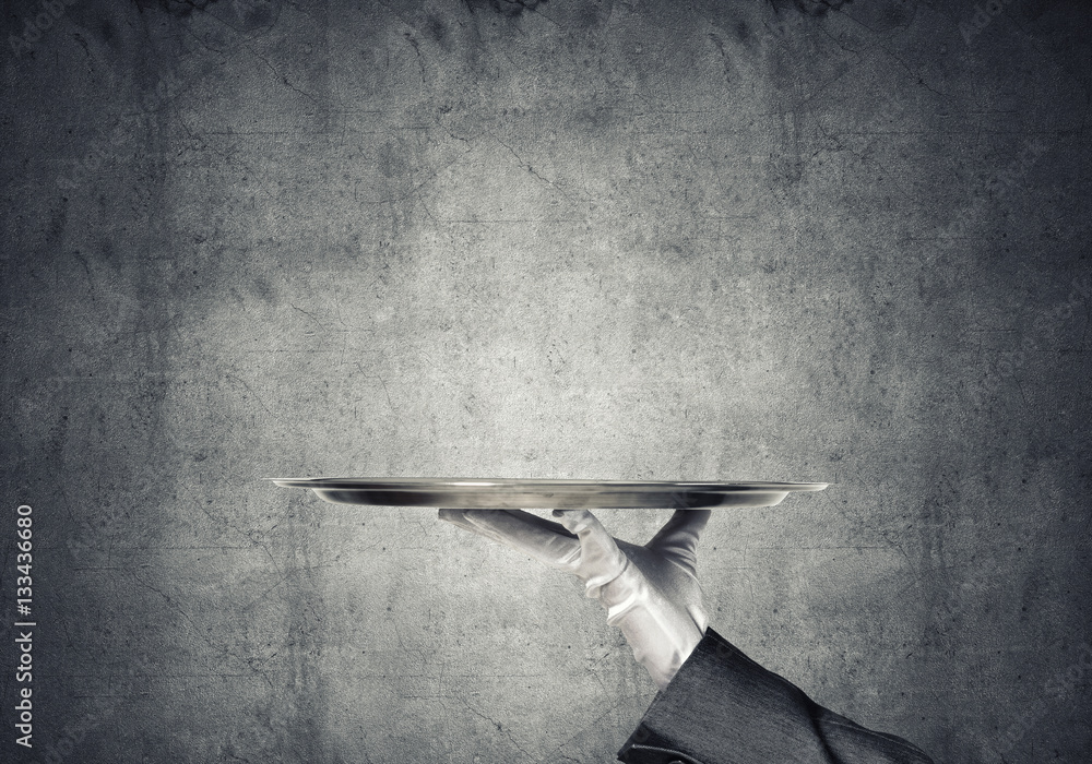 Hand of butler holding empty metal tray against concrete background