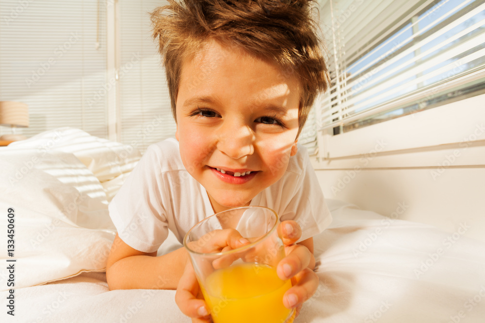 Happy boy with glass of fresh juice in his bedroom