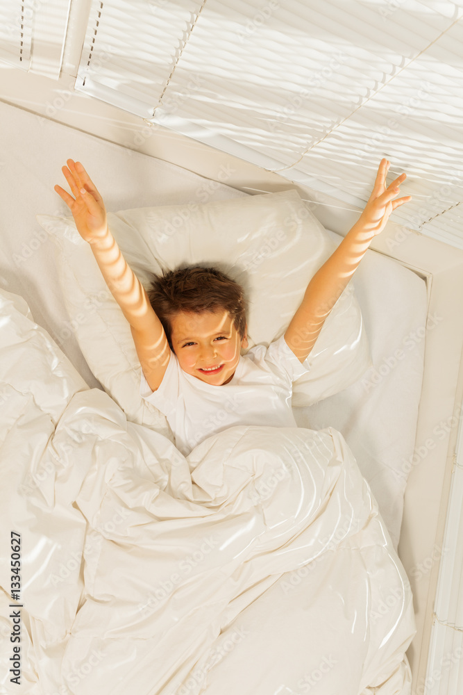 Peppy kid boy waking up in his white bedroom