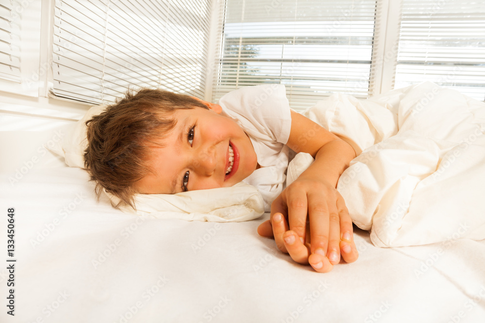 Smiling boy lying in his bed looking at camera