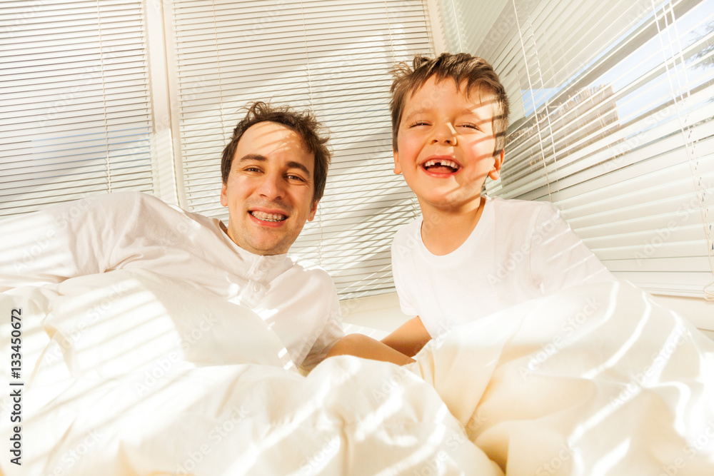 Happy father and kid boy laughing in bed