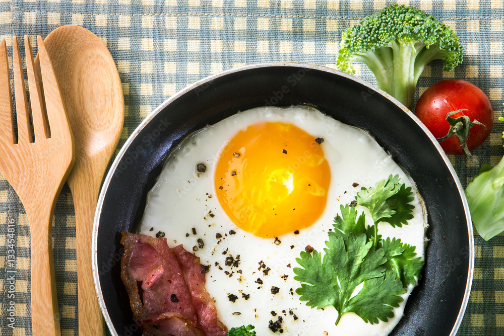 Breakfast with fried egg and bacon in dark pan on the table