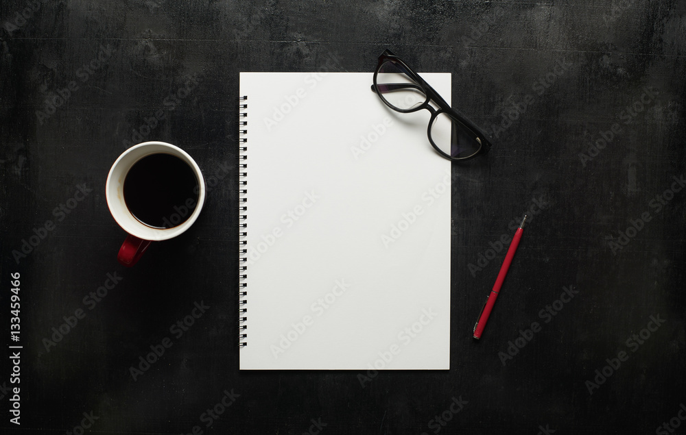 Wooden black office desk table with eyeglasses, notebook and pen with cup of coffee. Blank notebook 