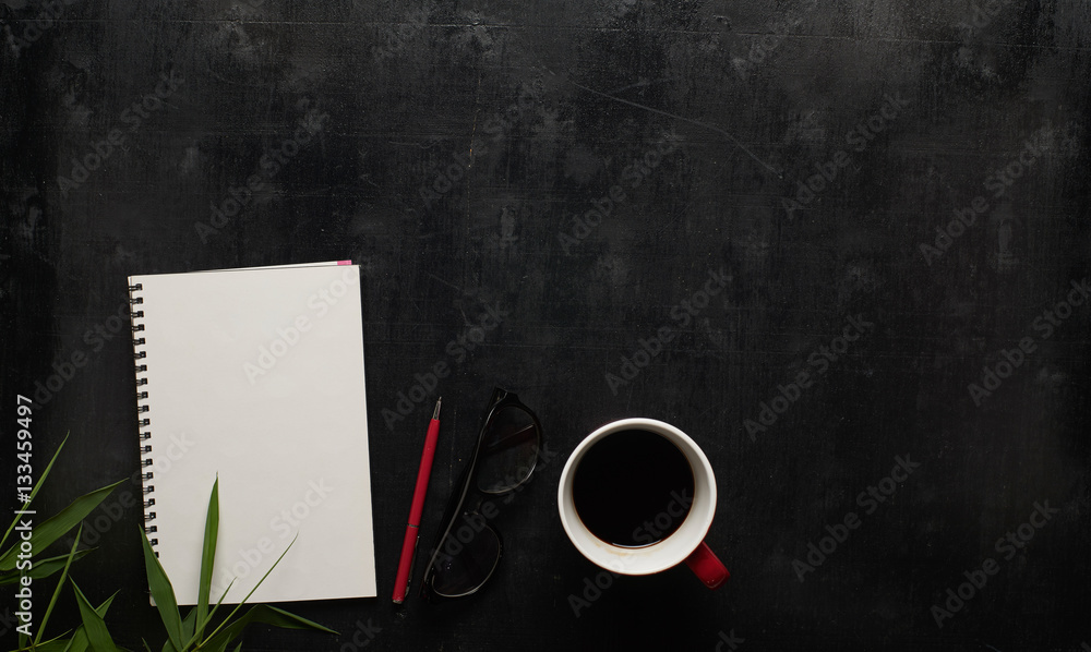 Wooden black office desk table with eyeglasses, notebook and pen with cup of coffee. Blank notebook 