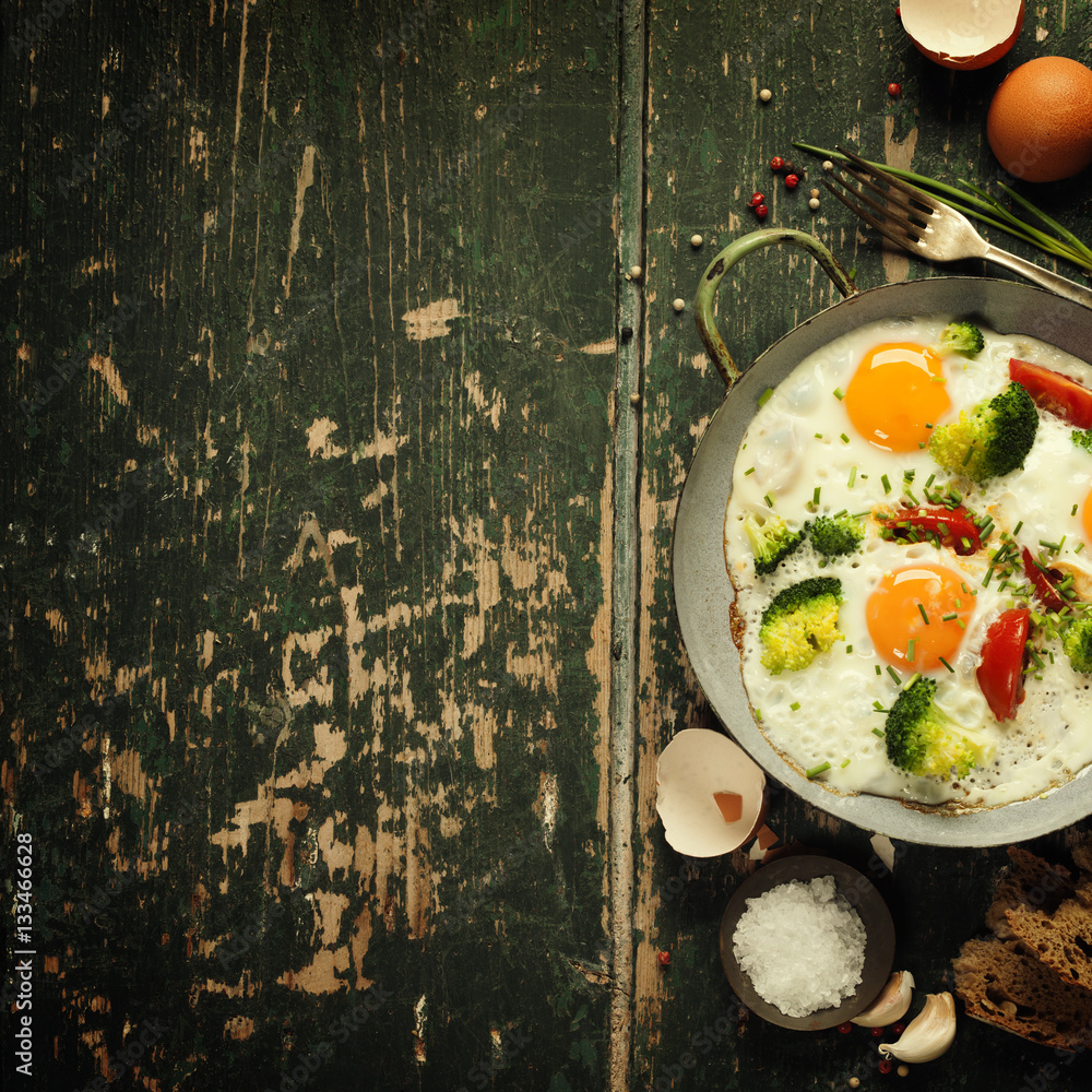 Pan of fried eggs, broccoli and cherry-tomatoes, top view