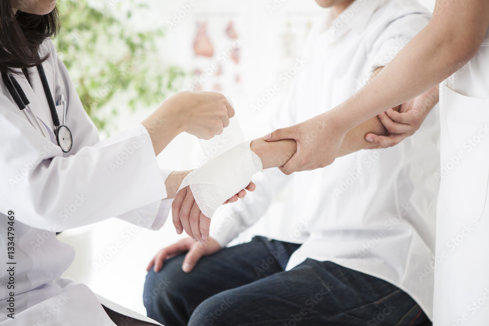 The doctor is wrapping a bandage in the hand of a man