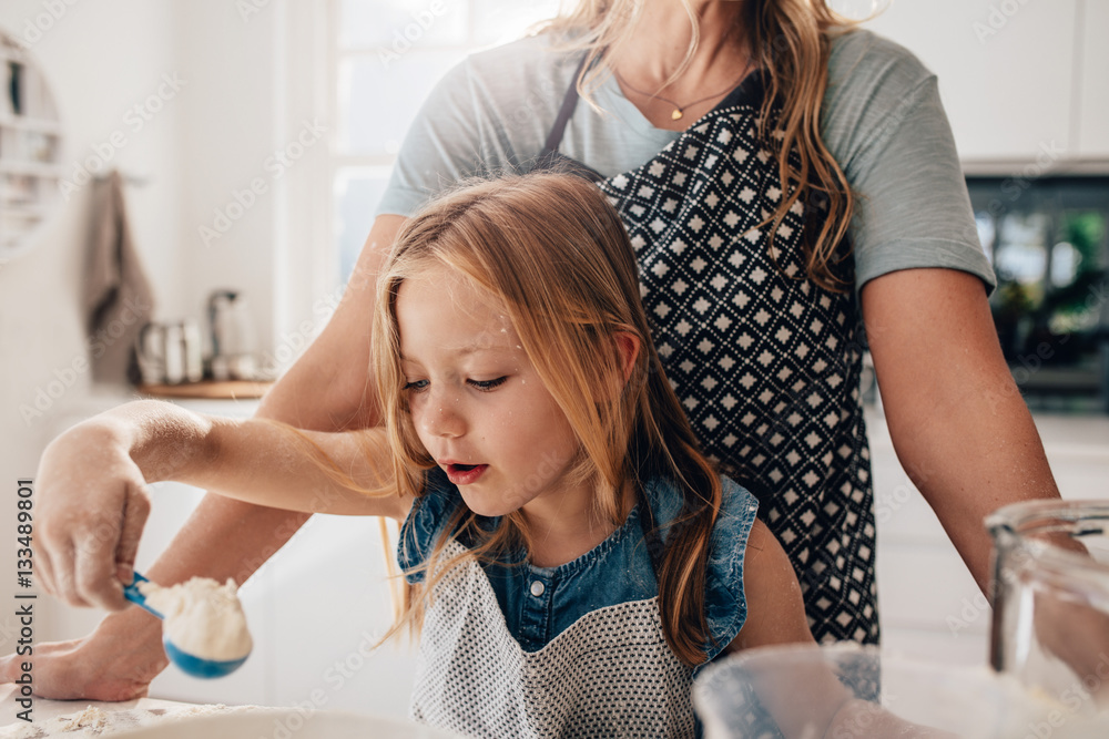 Little girl mixing batter in kitchen with her mother