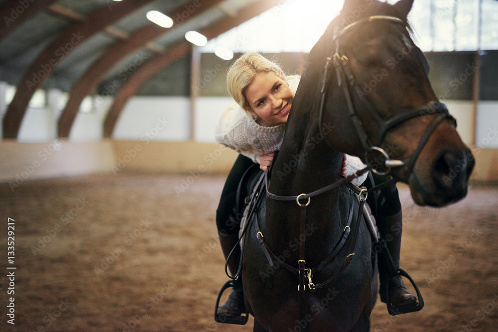 Smiling blonde female leaning on black horseback