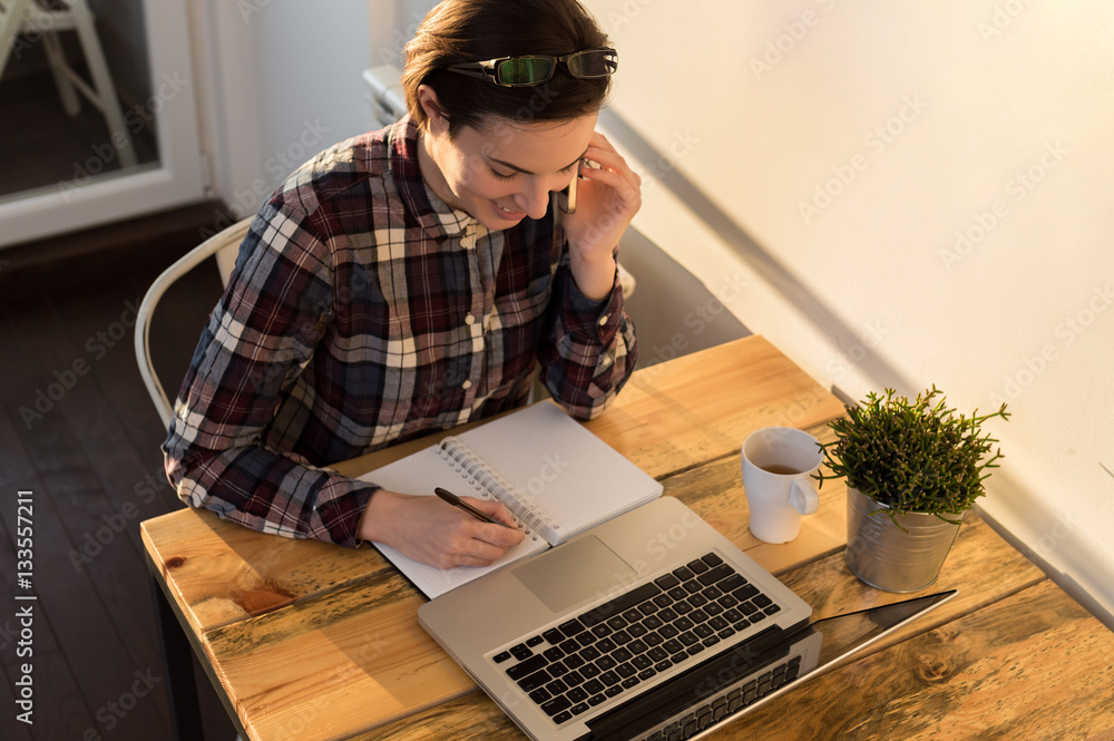 Top view of woman talk to cellphone when using the laptop comput