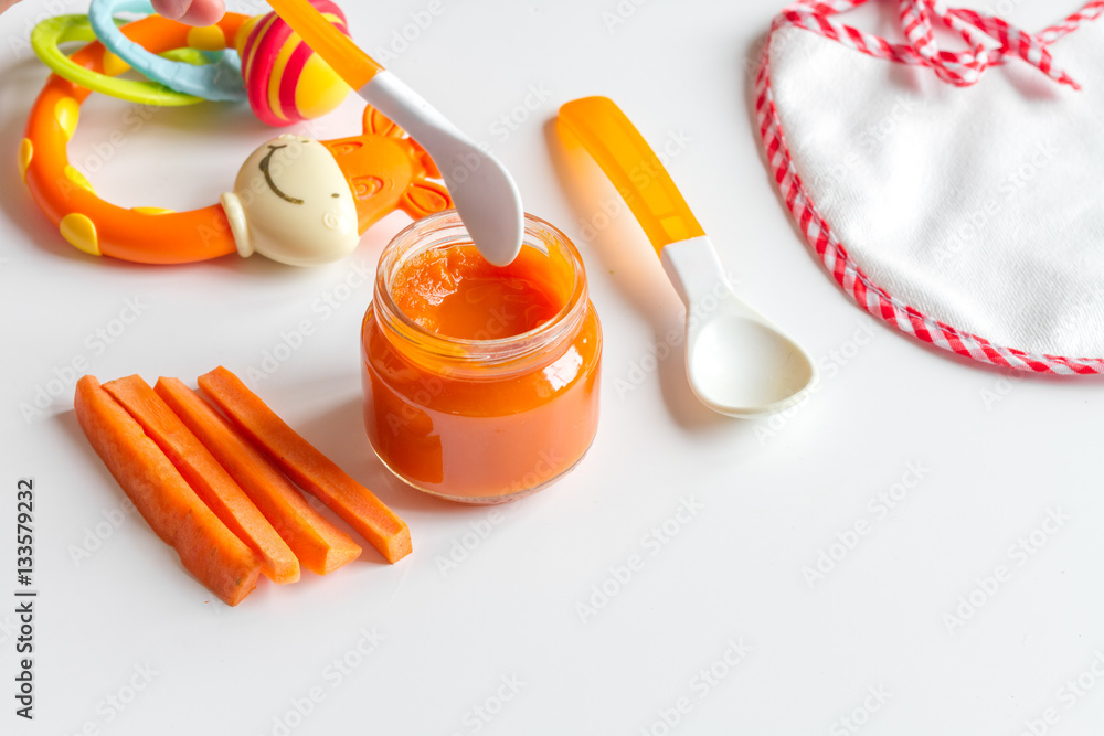 baby mashed with spoon in glass jar on white background