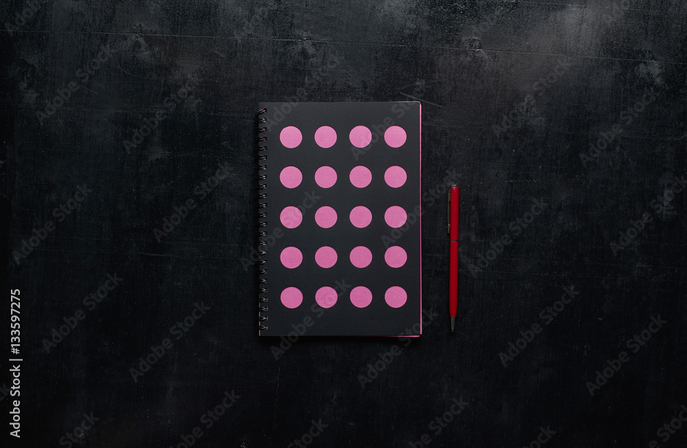 Wooden black office desk table with notebook and red pen . Top view