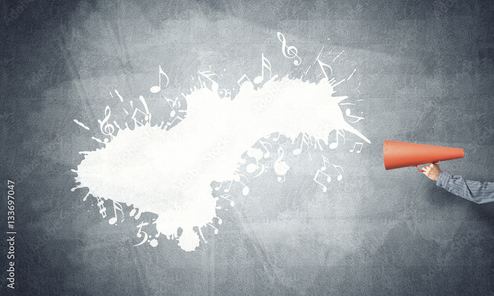 Hand of man holding orange paper trumpet against concrete background