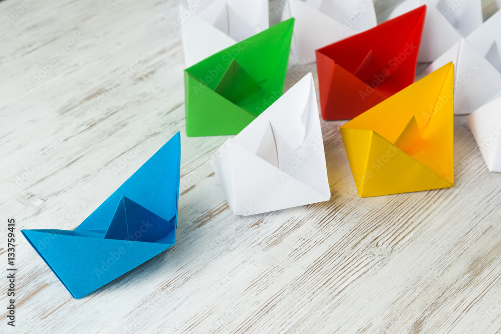 Business leadership concept with white and color paper boats on wooden table