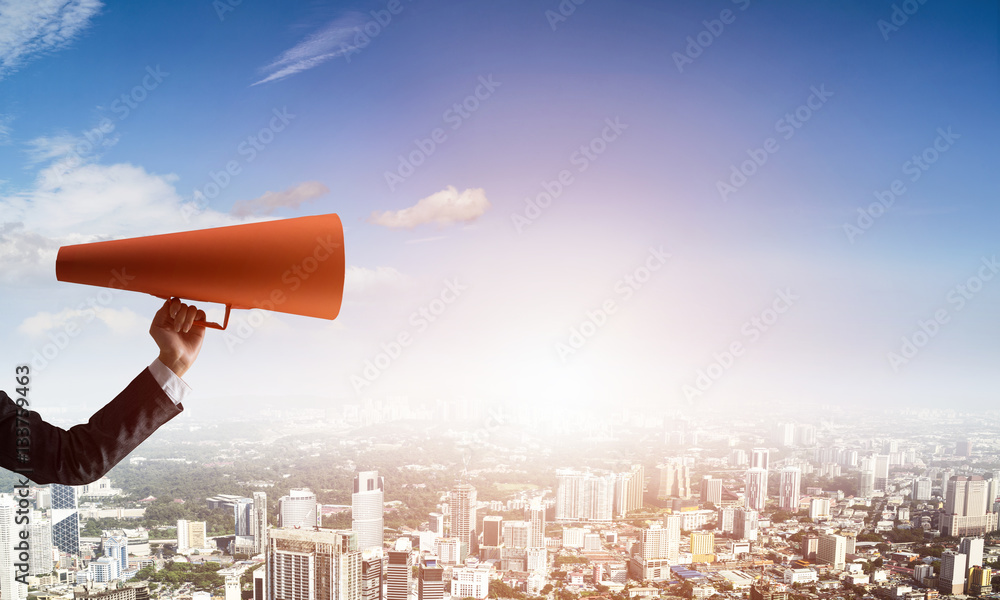 Hand of businesswoman holding red paper trumpet against cityscape background