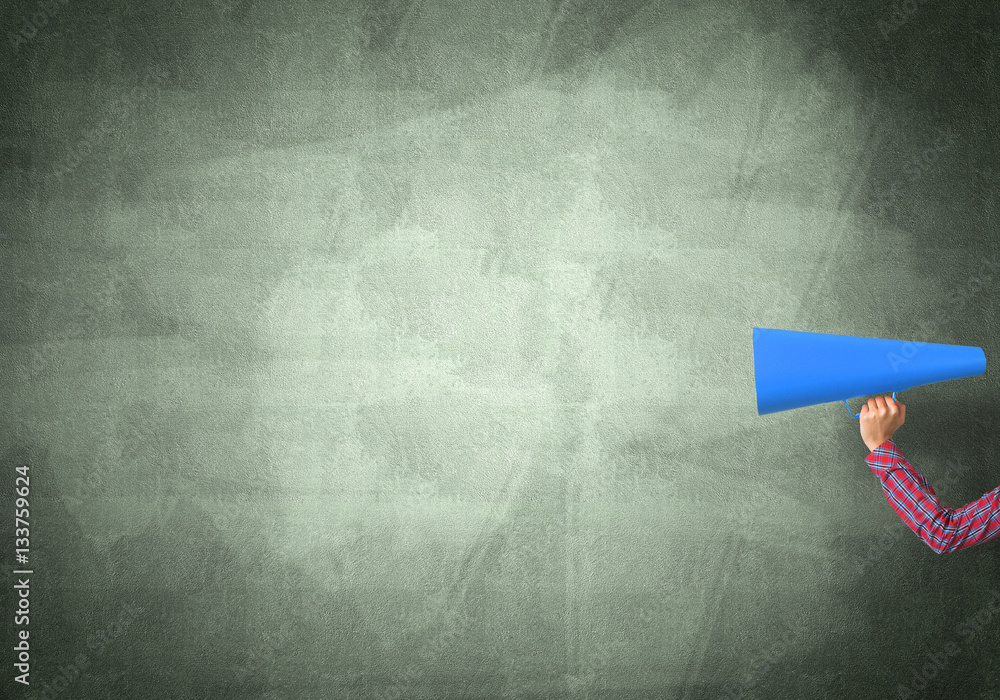 Hand of woman holding paper trumpet against concrete background