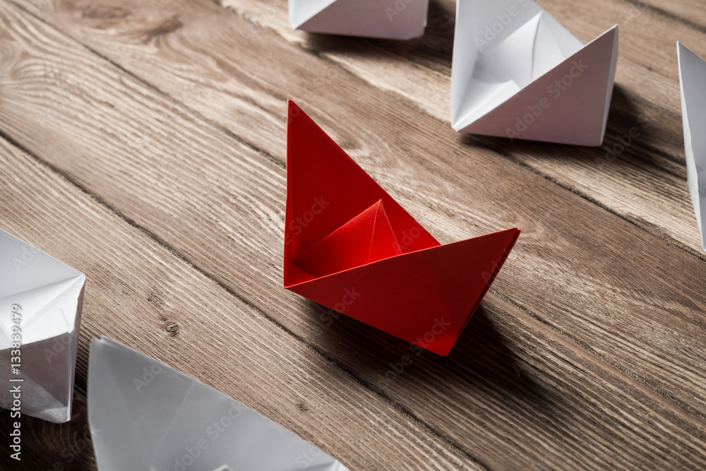 Business leadership concept with white and color paper boats on wooden table