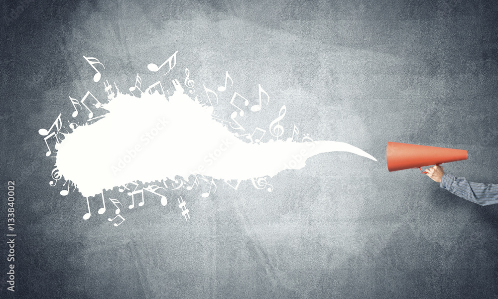 Hand of man holding orange paper trumpet against concrete background