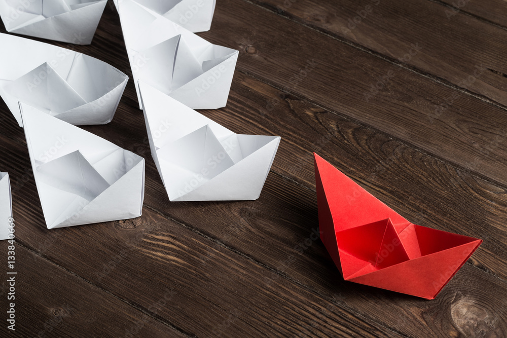 Business leadership concept with white and color paper boats on wooden table