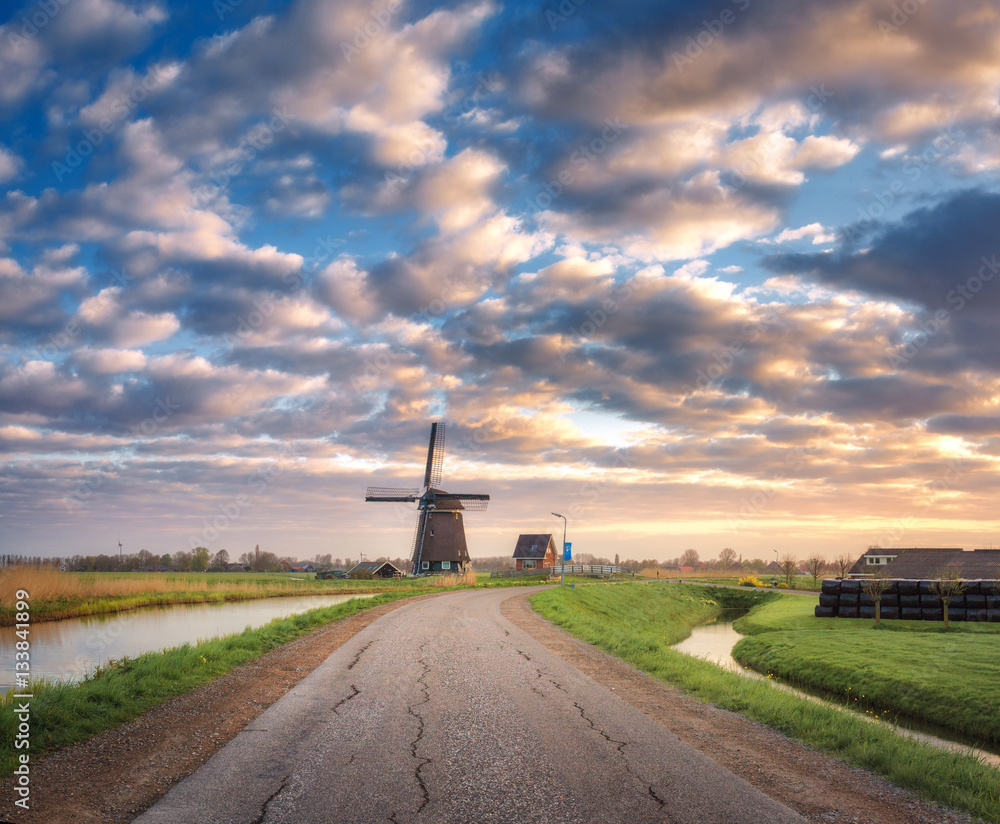 Road with windmill at sunrise in Netherlands. Beautiful old dutch windmill against colorful sky with